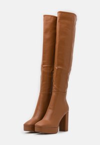 Bottes en faux cuir marron montantes, avec un talon épais, une semelle à plateforme et un zip sur le côté. Texture lisse et design épuré.