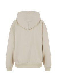 Beige huppari, jossa on kiristettävä huppu, ribbaatut hihat ja helma sekä sileä tekstuuri. Suunnittelussa on rento istuvuus ja minimaalinen yksityiskohtaisuus.