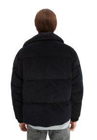 Giacca imbottita in velluto a coste di un blu navy scuro con colletto alto, polsini elastici e vestibilità rilassata, caratterizzata da sezioni orizzontali trapuntate.