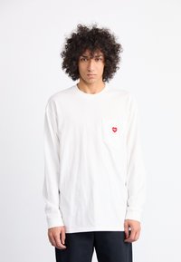 Long-sleeve white t-shirt made of cotton, featuring a red heart logo on the left chest pocket. Simple design with a relaxed fit.