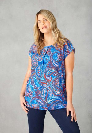 Korte mouwen blauwe top met een paisleypatroon in rood en wit, met een ronde hals en een relaxte pasvorm. Gecombineerd met donkerblauwe broek.