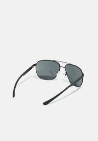 Ochelari de soare stil aviator cu un cadru metalic negru, lentile gri și brațe din cauciuc negru. Include suporturi pentru nas ajustabile pentru confort.