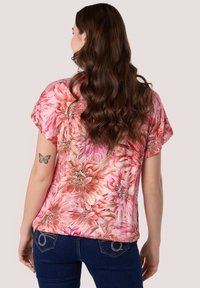 Roze bloemenblouse met korte mouwen, een losse fit en levendige bloemmotieven, gecombineerd met donkerblauwe jeans met decoratieve achterzakken.