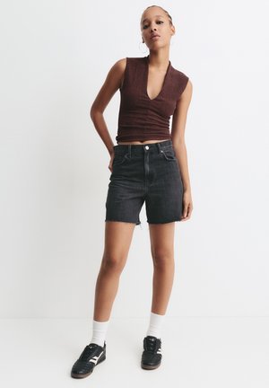Mørk denim shorts med frynset kant, parret med en tætsiddende ribbet brun top. Modellen har sorte sneakers med hvide såler og crew-sokker på.