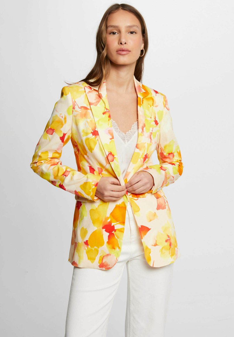 Blazer floral con patrones en acuarela de color amarillo, naranja y rosa sobre un fondo blanco. Diseño entallado con solapas con muesca y mangas largas.