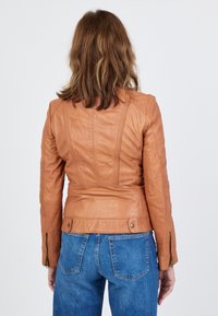 Brun läderjacka med en åtsittande design, kviltade axlar och sidodragkedjor. Bärs över högmidjade blå jeans.