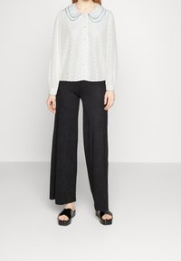 White textured blouse with a large blue-trimmed collar, button closure, paired with wide-leg black trousers and black slide sandals.