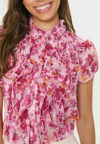 Floral blouse featuring a frill design in shades of pink with orange accents, short sleeves, and a button-down front. Lightweight, textured fabric.