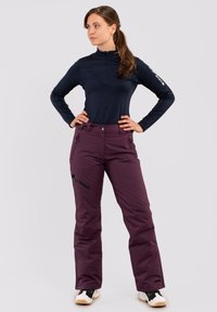 Marineblauw lichtgewicht longsleeve shirt met halve rits en paarse geïsoleerde broek met ritszakken en een getailleerde pasvorm. Zwart-witte schoenen.