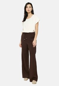 Top corto a maniche corte color crema abbinato a pantaloni marroni a vita alta e gamba larga con cordoncino e dettagli dorati. Footwear beige completa il look.