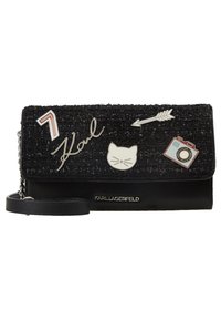 Borsa nera con un frontale in tessuto testurizzato decorato con vari dettagli metallici, tra cui accenti a forma di gatto, freccia e macchina fotografica.