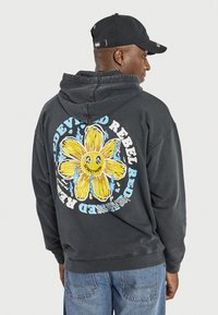 Felpa nera con cappuccio, caratterizzata da una grande grafica di un fiore colorato sul retro, con il testo "DEVIL" e "REBEL" in lettere grasse.