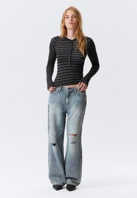 Black and gray striped long-sleeve top with button placket, paired with light blue distressed wide-leg jeans and black pointed-toe shoes.