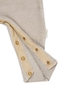 Beige knitted fabric with a snap button strip showing five brass-colored fasteners and a small white tag with text.