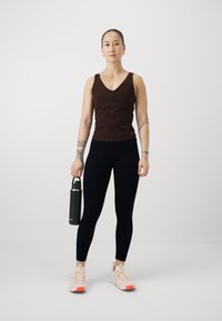 Ruda sportinė palaidinė su V formos iškirpte, derinama su juodais leggingais. Modelis laiko juodą vandens butelį ir dėvi šviesius batus su oranžiniais akcentais.