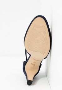 Chaussure à talon haut en daim bleu marine avec un bout pointu, présentant une semelle beige texturée et un accent de talon en caoutchouc noir. Détails de la marque Gabor visibles.