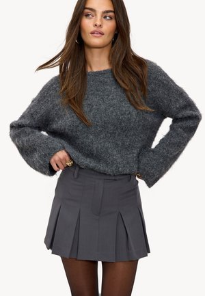 Un pull gris en peluche à manches longues, associé à une jupe plissée charbon. La tenue présente une finition texturée et un design ajusté.