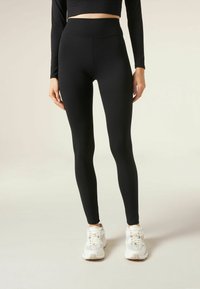 Svarta leggings i ett stretchigt, slätt material med hög midja; kombinerat med vita träningsskor.
