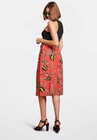 Rød midi nederdel med blomstermotiv, der har sorte og gule accenter, parret med en ærmeløs sort top og sorte hæle sandaler.