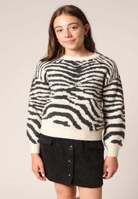 Gebreide trui in crème met zwarte zebra strepen, ronde halslijn en geribbelde manchetten. Gecombineerd met een zwarte mini-jurk met knopen en zakken.