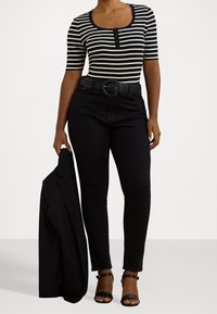 Černobíle pruhovaný top s krátkým rukávem a detaily na knoflících, spárovaný s černými přiléhavými džíny, tkaným pásem a černými podpatky. Drží černý blazer.