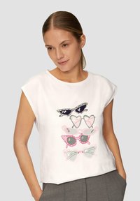 Biała koszulka krótki rękaw z kolorową grafiką przedstawiającą różne okulary przeciwsłoneczne w odcieniach zieleni, różu i czerni. Wykonana z miękkiej bawełny.