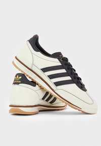 Witte en zwarte Adidas sneakers met gumzolen, zwarte veters en het Adidas-logo in goud op het hielstuk en de tong.