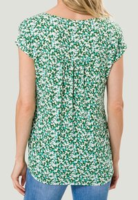 Blusa corta de manga corta con estampado floral en verde, con un diseño de espalda fruncida, patrones en azul claro y blanco, tejido suave y un corte relajado.