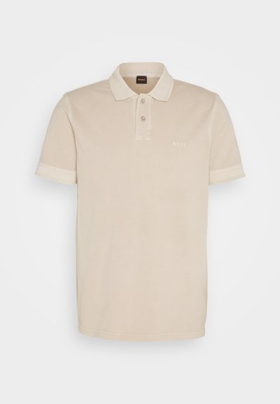 Polo beige en coton doux. Il présente un col classique, deux boutons et un petit logo brodé sur la poitrine.