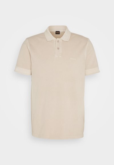 Polo beige en coton doux. Il présente un col classique, deux boutons et un petit logo brodé sur la poitrine.