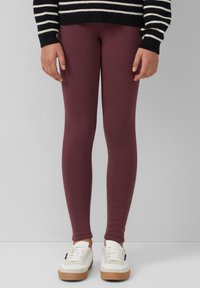 Bordeaux leggings gemaakt van zachte, rekbare stof, aansluitend ontwerp, gecombineerd met witte sneakers met bruine zolen. Gestreepte zwart-witte trui.