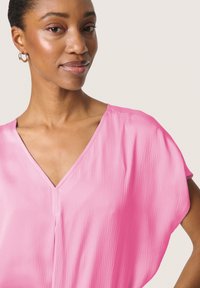 Blusa rosa de escote en V con mangas cortas y drapeadas. La tela tiene una sutil textura con un acabado suave. Sin patrones visibles ni adornos.