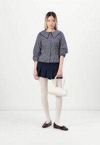 Blusa a quadri blu con grande colletto, maniche a sbuffo, gonna plissettata blu, borsa bianca, collant crema e ballerine bordeaux.