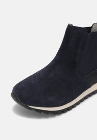 Bottine en daim bleu foncé avec panneau latéral élastique noir, semelle intermédiaire blanche et semelle extérieure en caoutchouc noir crantée.