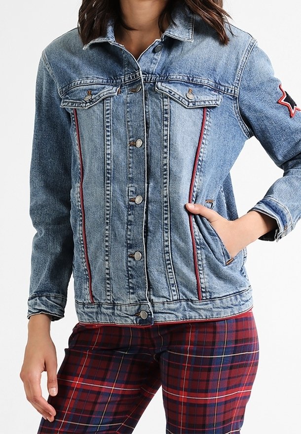 Jeansjacka med ljusblå tvätt, röda sidsömmar, knäppning med knappar, två bröstfickor och ett stjärnmärke på höger ärm.