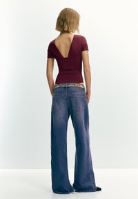 Bordový priliehavý top s hlbokým výstrihom do V na chrbte, v kombinácii so širokými modrými rifľovými nohavicami so strieborným opaskom s cvokmi a dvomi zadnými vreckami.