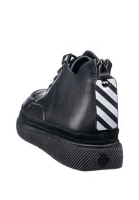 Stivaletto in pelle nera con suola testurizzata, dotato di una cerniera sul retro e un dettaglio a strisce bianco e nero.