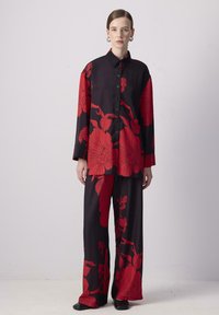 Schwarzes Stoffoutfit mit kräftigem roten Blumenmuster, bestehend aus einem langärmeligen Hemd mit Knöpfen und weit geschnittenen Hosen, glatte Textur, lässige Passform.