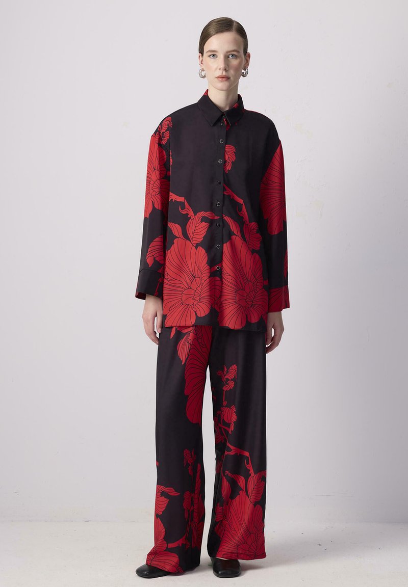Schwarzes Stoffoutfit mit kräftigem roten Blumenmuster, bestehend aus einem langärmeligen Hemd mit Knöpfen und weit geschnittenen Hosen, glatte Textur, lässige Passform.