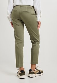 Pantalons slim olive avec poches arrière, assortis à des chaussures de style sneaker multicolores. Le tissu semble lisse avec une texture minimale.