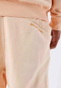 Sudadera de melocotón claro y pantalones a juego con tela texturizada. Los pantalones cuentan con un bolsillo parche y un pequeño logo en relieve en un tono contrastante.