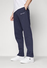 Navy blue sweatpants made of cotton, featuring a logo on the left thigh, side pockets, and a relaxed fit with cuffed hems.