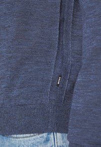 Pulover tricotat de culoare bleumarin, cu manșete și tiv cu nervuri, având un mic eticheta din țesătură neagră cu „BOSS”. Design texturat, casual.