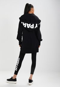 Black hoodie with oversized fit, white "Y PARK" text on the hood, paired with black leggings featuring "IVY PARK" in white. Black footwear included.