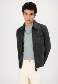 Sort læderjakke med lynlås front, skjortekrave og to sidelommer. Båret over en grå t-shirt og parret med off-white bukser.