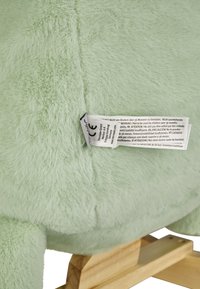 Green plush toy with a soft, fuzzy texture, featuring a wooden base and a care label attached, displaying care instructions.