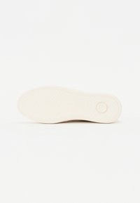 Sko såle med en strukturert overflate, laget av lys beige gummi. Har et sirkulært logo og en glatt finish rundt kantene.