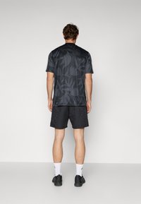 Black athletic t-shirt with a subtle leaf pattern, paired with black shorts featuring a textured design. White socks and black shoes complete the outfit.