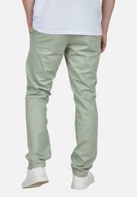 Pantalons en coton vert clair à coupe droite et texture lisse, associés à des baskets blanches. La vue arrière montre un léger affinage au niveau de la cheville.