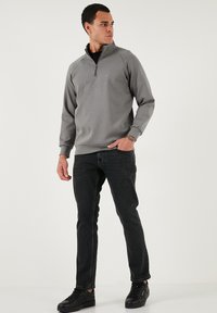 Šedá mikina s kapucí na zip, dlouhými rukávy, žebrovanými manžetami a rovním lemem, v kombinaci s černými džíny a černými teniskami. Hladká textura.